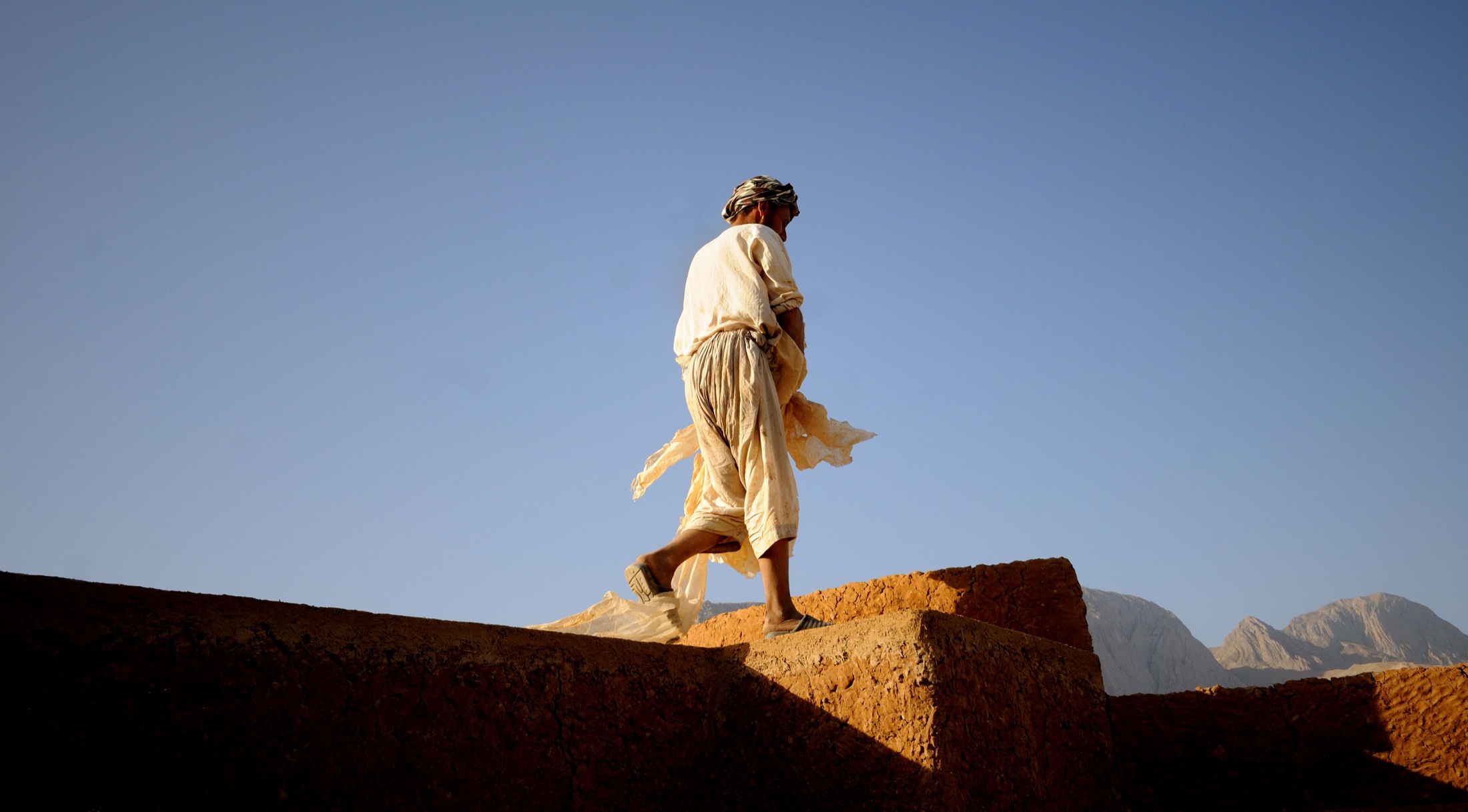 A local heritage worker walking along an earthen wall in Kholm, Afghanistan